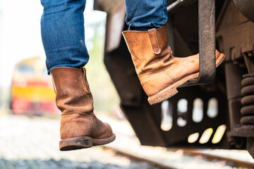 Action of a man wearing leather safety shoe is climbing up on the train locomotive driver cabin ladder. Transportation industrial working action scene. Close-up and selective focus.