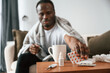 Holding pills that are on the table. Sick black man is at home