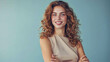 © Studio Nova - woman with curly hair is smiling at the camera, standing with her arms crossed in front of a light blue background