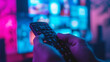 close-up view of a hand holding a television remote control with a blurred television screen in the background, displaying colorful images.