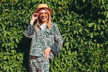 Young beautiful smiling blond hipster woman in trendy summer hippie costume clothes. Carefree female posing in the street at sunny day. Positive model outdoors at sunset. Cheerful and happy in hat