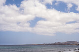 Fototapeta Morze - Seascape. Large white clouds. Mountains in the background. Rocky beach, turquoise Atlantic Ocean. Village of Arrieta. Lanzarote, Canary Islands, Spain