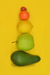 Pyramid of fruits and vegetables on a yellow background, abstraction, avocado, apple, lemon,  tangerine and tomato.  