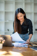 © Wasana - Cheerful businesswoman reviewing a financial report next to her laptop in a well-lit office space..