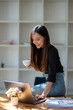 © Wasana - Smiling businesswoman holding a cup of coffee while working on her laptop in a contemporary office space..