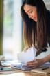© Wasana - Close up hands of cheerful businesswoman reviewing a financial report next to her laptop in a well-lit office space.