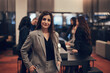 © Flamingo Images - Confident businesswoman standing in an office lobby with colleagues in the background