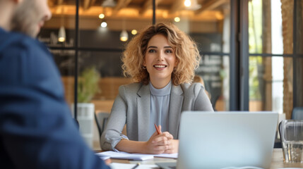 Poster - A professional woman is conversing with a colleague in an office setting, with a laptop open in front of them, suggesting a business meeting