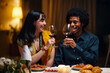 © DragonImages - Happy young man and woman with glasses of red wine toasting for love and Valentine Day while sitting by served table at dinner