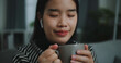 © Johnstocker - Portrait of Happy young asian woman enjoy listening to the music with wireless headphones while sitting drink coffee on sofa in living room at home, Leisure and lifestyle,Free time