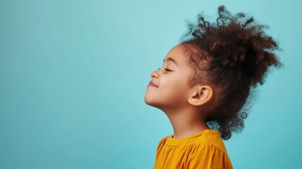 Wall Mural - A young child with curly hair wearing a yellow top looking up with a smile against a light blue background.