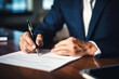 © Wararat - Close up hand of businessman in suit writing business papers at desk in modern coworking office.