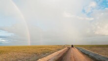 Rainbow Over The Road. Immerse Your Audience In The Breathtaking Beauty Of A Rainbow Gracing The Open Road, Flanked By Picturesque Fields, And Meandering Through A Safari Park