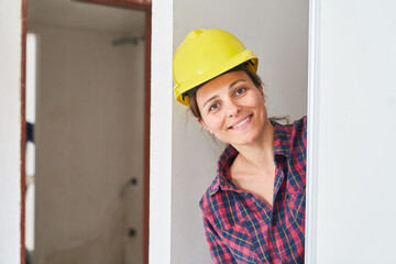 Portrait of smiling young female construction worker wearing safety workwear installing door at incomplete house