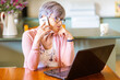 © Austockphoto - Mature woman on laptop at home using mobile phone to call for tech support