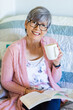 © Austockphoto - Happy woman reading a book while drinking a cuppa tea