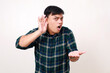 © ArvStd - I can’t hear you! Young asian man holding hand above ear asking to be louder over white background
