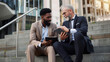 © Santy Hong - Tablet, conversation and business men in the city in discussion for corporate legal case. Teamwork, collaboration and male attorneys with digital technology sitting and talking on stairs in town.