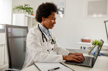 Wall Mural - Female doctor sitting at her office in front of laptop computer doing consultations online over internet.