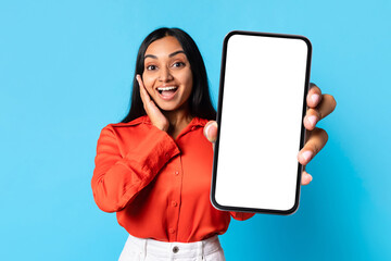 Excited Indian woman shows large phone with blank screen, studio