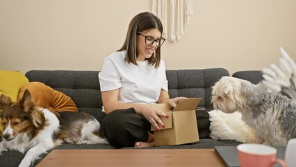 Canvas Print - Hispanic woman unboxing a package on a sofa with two attentive dogs in a cozy living room.