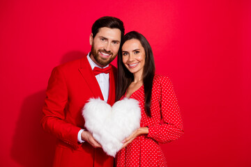 Poster - Portrait of lovely peaceful partners arms hold comfy fluffy heart figure pillow empty space isolated on red color background