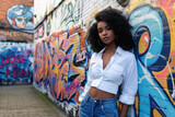 Fototapeta  - A curly-haired girl stands in front of a bright graffiti wall