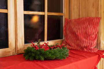 Wall Mural - Decorated Xmas wreath with candle and pillow on a windowsill. Comfort. Cozy Scandinavian decor of the room. Christmas Wreath of fir branches near window. Festive decoration at home	