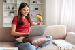 © Prostock-studio - Beautiful young asian woman holding credit card while using laptop at home