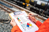 Fototapeta  - Action of an engineer is checking on chemical hazardous material checklist form with background of train freight tanker for crude oil or chemical cargo. Industrial safety working scene. 