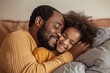 © Tanya - Happy smiling afro american father and daughter lying on the sofa and hugging. Father's day concept.