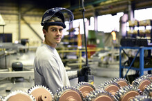 Portrait Of Young Smiling Industrial Worker With Helmet In A Modern Industrial Hall At His Workplace