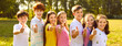 © Studio Romantic - Cheerful kids enjoy summertime and spend free time on green meadow on good summer day. Banner header background with group of happy children standing in row showing thumbs up okay satisfaction gesture
