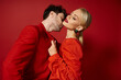 © LIGHTFIELD STUDIOS - blonde woman in dress and red earrings seducing handsome man on red background, fashionable couple