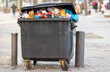 Überquellender Müllcontainer, der auf der Straße steht und auf seine Abholung durch die Müllabfuhr wartet