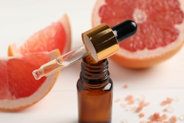 Grapefruit essential oil in bottle, pipette and fruit on white table, closeup