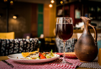 Wall Mural - Greek salad and glass of red wine on the oak table