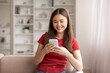 © Prostock-studio - Delighted young asian woman typing message on her smartphone and smiling