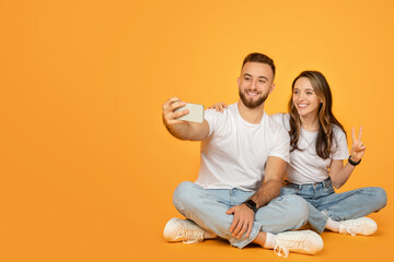 Poster - A young, seated couple happily engaged in taking a selfie, with the man holding the phone