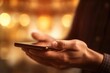 © gankevstock - closeup hands gracefully holding a smartphone, highlighted by the warm and inviting glow of ambient lights in the background