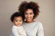 © FoxTok - Happy motherhood, family, love. Young beautiful smiling African American woman with a baby in her arms on beige background, portrait. Black girl with child, mother's day