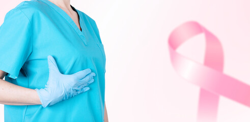 Wall Mural - A female doctor in a medical uniform supports her breasts and a pink ribbon as a symbol of breast cancer awareness. Medical pink background. Poster. copy space.