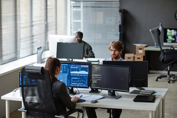 High angle view at young IT developers working with multiple computer monitors in open office copy space