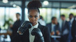 Black businesswoman in office wearing red boxing gloves, looking determined
