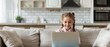 Cheerful little girl using laptop while sitting on sofa at home