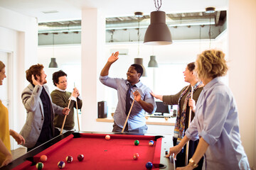 Canvas Print - Group of coworkers playing pool and celebrating in a modern office break room