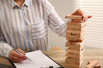 Wall Mural - Playing Jenga. Woman building tower with blocks at wooden table in office, closeup