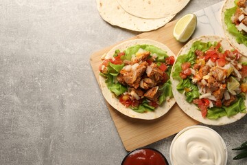 Delicious tacos with vegetables, meat and sauce on grey textured table, flat lay. Space for text
