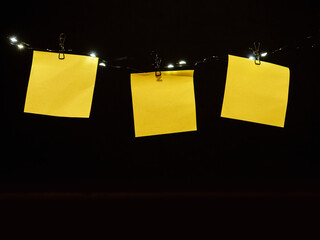 Three yellow blank note paper hanging on a string with lights. Dark background. Blank space for text or message. New year resolution concept. Setting up target and goals. Write dream to achieve