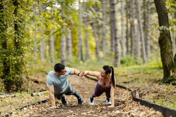 Wall Mural - Sportspeople are doing planks in nature and giving high five.